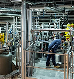 ASI - Recherche à l'application industrielle Technicien travaillant dans un atelier semi-industriel entouré de cuves et de tuyauteries métalliques - ITERG