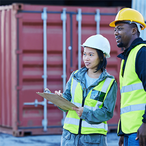 Groupe de professionnels en discussion sur un site logistique avec des conteneurs en arrière-plan.