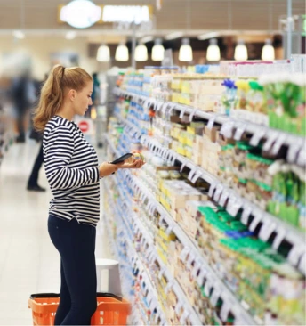 Femme scannant un produit alimentaire dans un rayon de supermarché, devant une étagère de produits emballés.