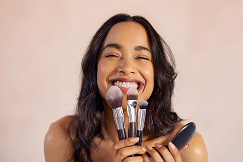 Masuillage naturel - modifications chimiques ITERG Femme souriante tenant des pinceaux de maquillage naturel - Cosmétique naturelle ITERG