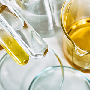 Vue rapprochée de verrerie de laboratoire avec des éprouvettes et béchers contenant des liquides transparents et dorés, utilisés en formulation.