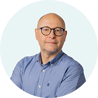 Portrait de Franck Dejean, bras croisés, portant une chemise bleue et des lunettes."