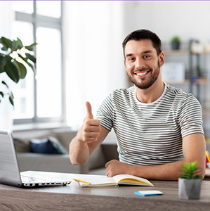 Homme travaillant sur ordinateur à domicile-ALLIANCE "Homme souriant devant son ordinateur portable, levant le pouce en signe d’approbation