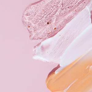 Produits cosmétiques naturels disposés sur fond rose, avec des pots de crème, flacons, savon solide et feuilles de plantes vertes.