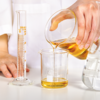 Personne versant un liquide huileux doré dans un bécher en laboratoire cosmétique