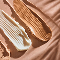 Goutte d’huile dorée tombant sur une surface de crème blanche texturée.