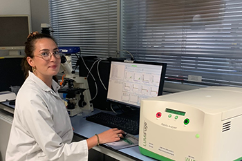 hercheuse en blouse blanche devant un poste informatique et un microscope, réalisant des analyses en laboratoire de formulation.</p>
<p>