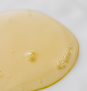 Pipette laissant tomber de l’huile jaune sur fond blanc.
